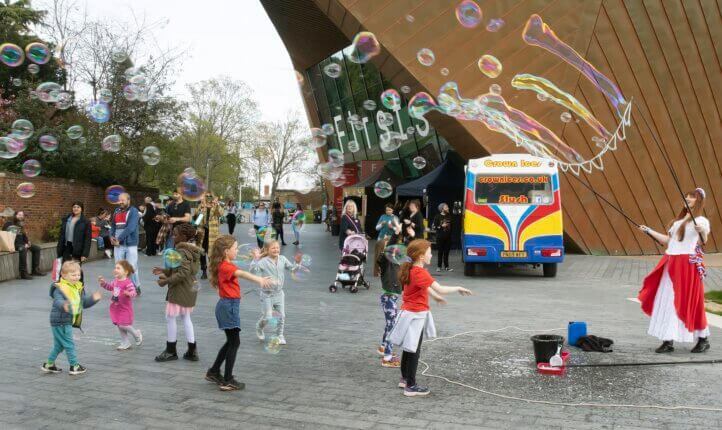 Children playing with a carnival artist creating bubbles blowing around in the air outside Colchester's Firstsite centre.