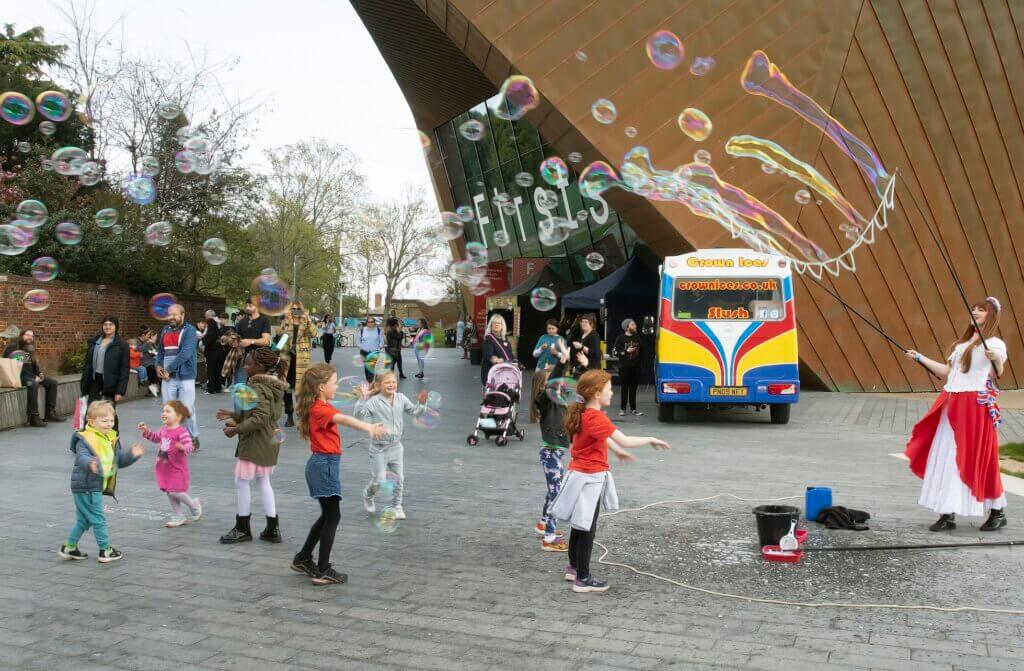 A group of children and a street entertainer playing with bubbles at Eastlight's community festival event